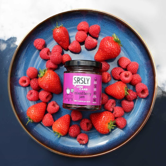 picture of SRSLY low card mixed berry jam jar on a plate surrounded by strawberries and raspberries